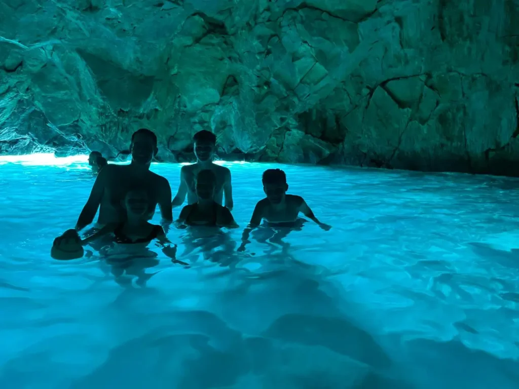 Group of visitors swimming inside the Blue Cave near Vlore, surrounded by glowing turquoise water and dramatic rocky cave walls illuminated by natural light from the cave entrance.