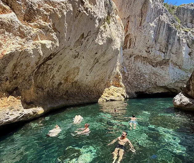 Visitors swimming in the Canyon of Smugglers on the Karaburun Peninsula, surrounded by towering limestone cliffs and crystal-clear emerald water within the narrow sea canyon.