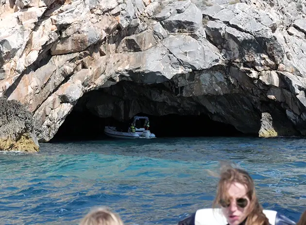 Entrance of Dafina Cave along the rocky coastline of the Karaburun Peninsula, with a small speedboat inside the dark sea cave and clear blue water in the foreground.