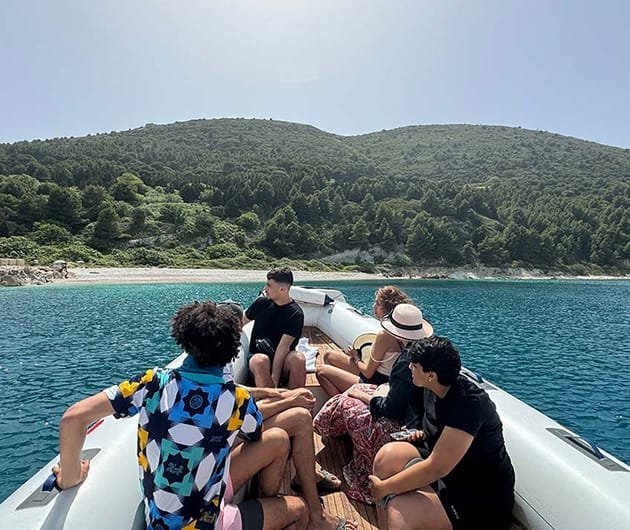 Group of visitors on a speedboat near Sazan Island, Albania, with clear blue sea in the foreground and the island’s green hills and forested coastline visible in the background.